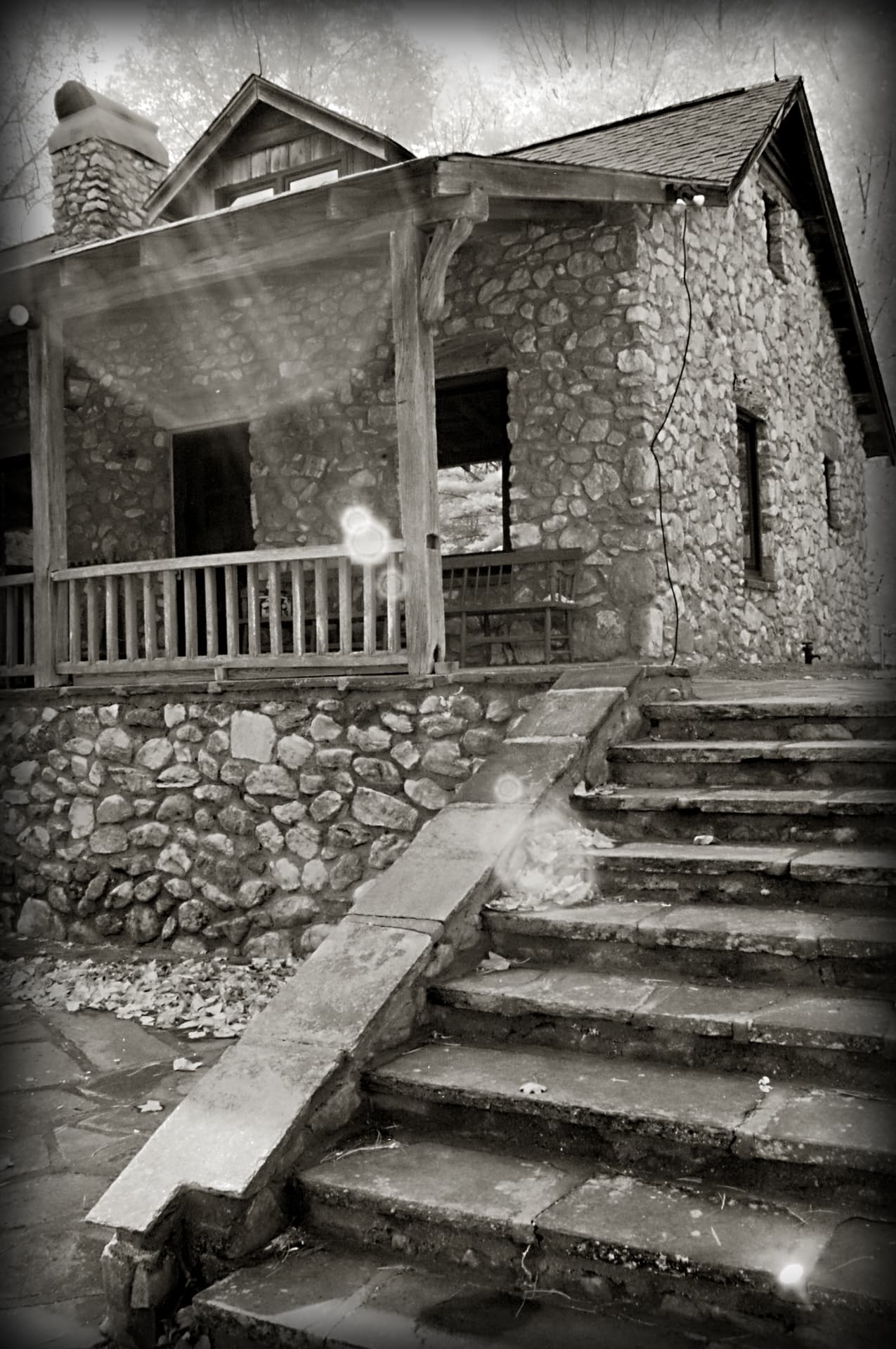 Black and white photograph of the stone steps rising to the Skeet House porch at Devotion, with its river rock walls, timber posts, and stone chimney