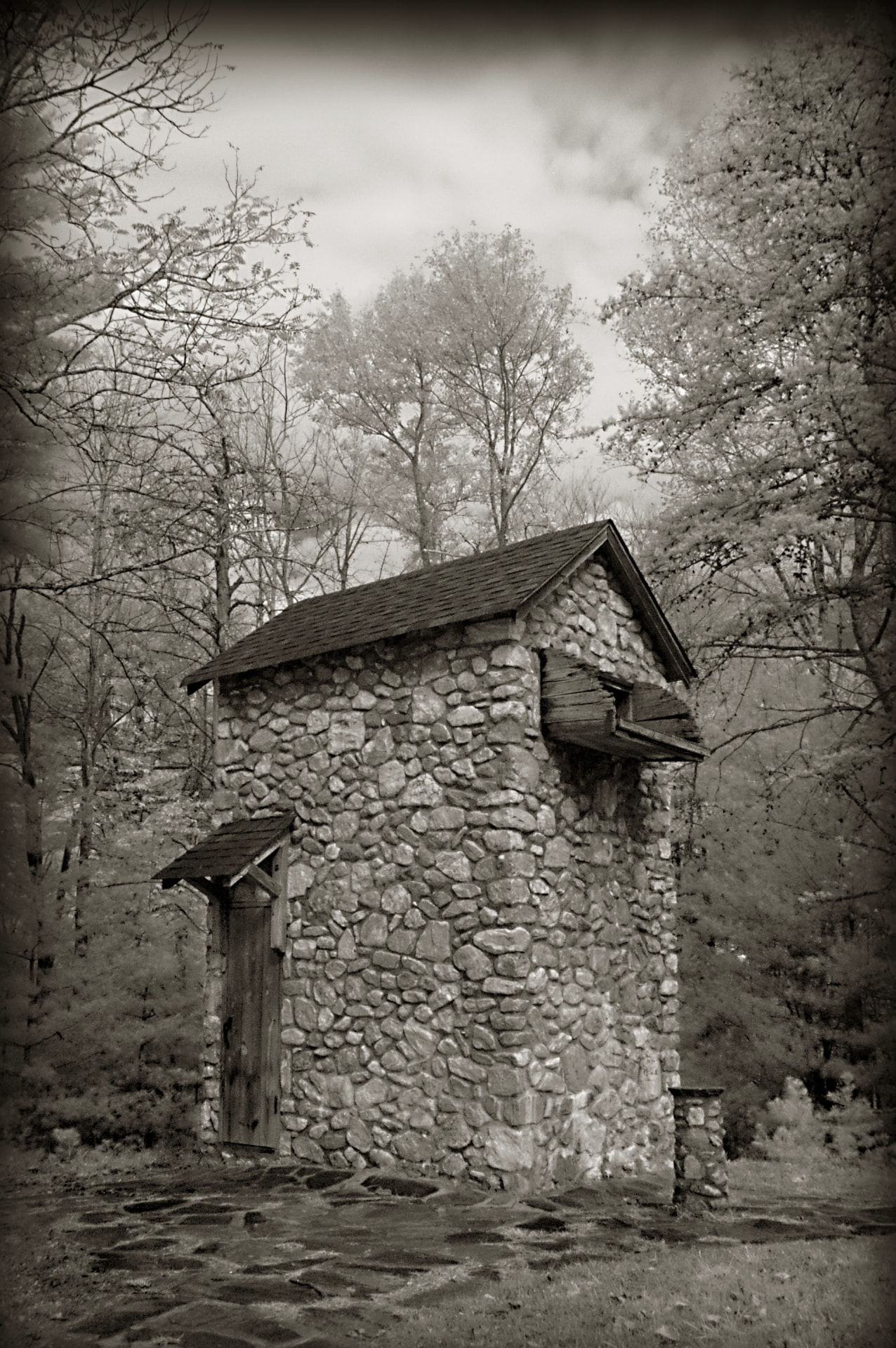 Black and white photograph of the tall stone high house at the Devotion skeet field, standing among bare trees with a shingled roof and timber door hood