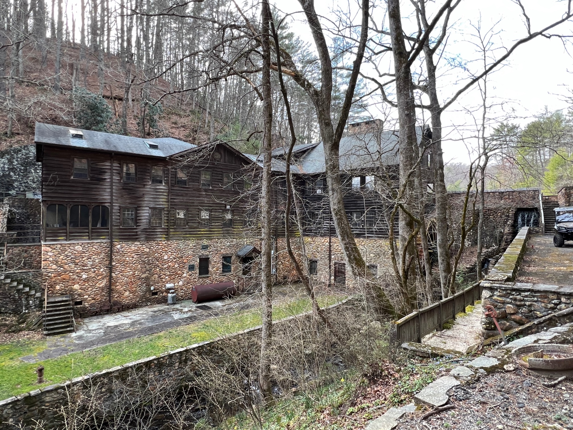 The chestnut-clad workshop range at Devotion on its river-rock foundation — the movie theater, woodworking shop, and metallurgy shop connected to the Lodge above the walled tailrace