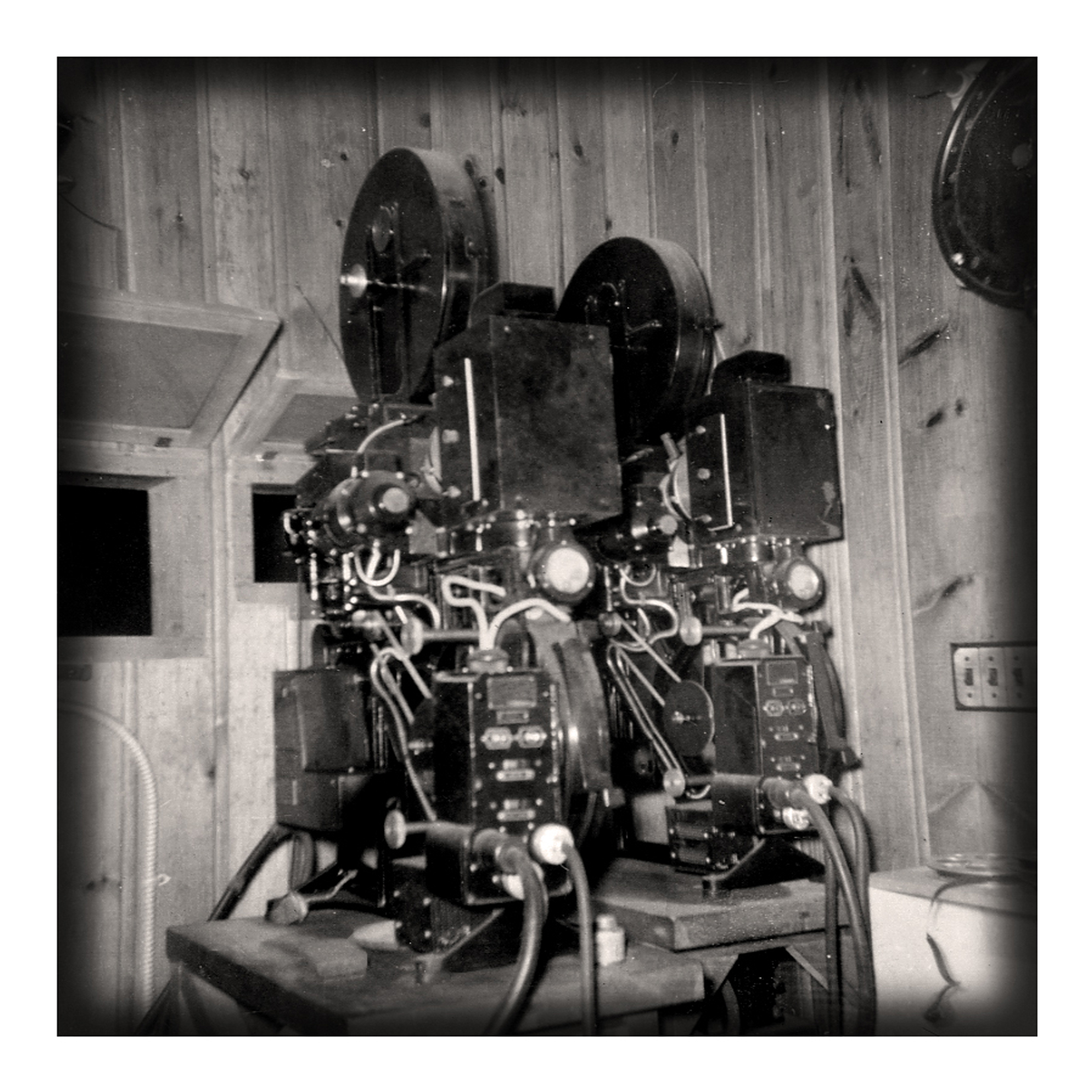 Paired 35mm film projectors with reel housings in the pine-panelled projection booth of the Lodge's movie theater, 1953