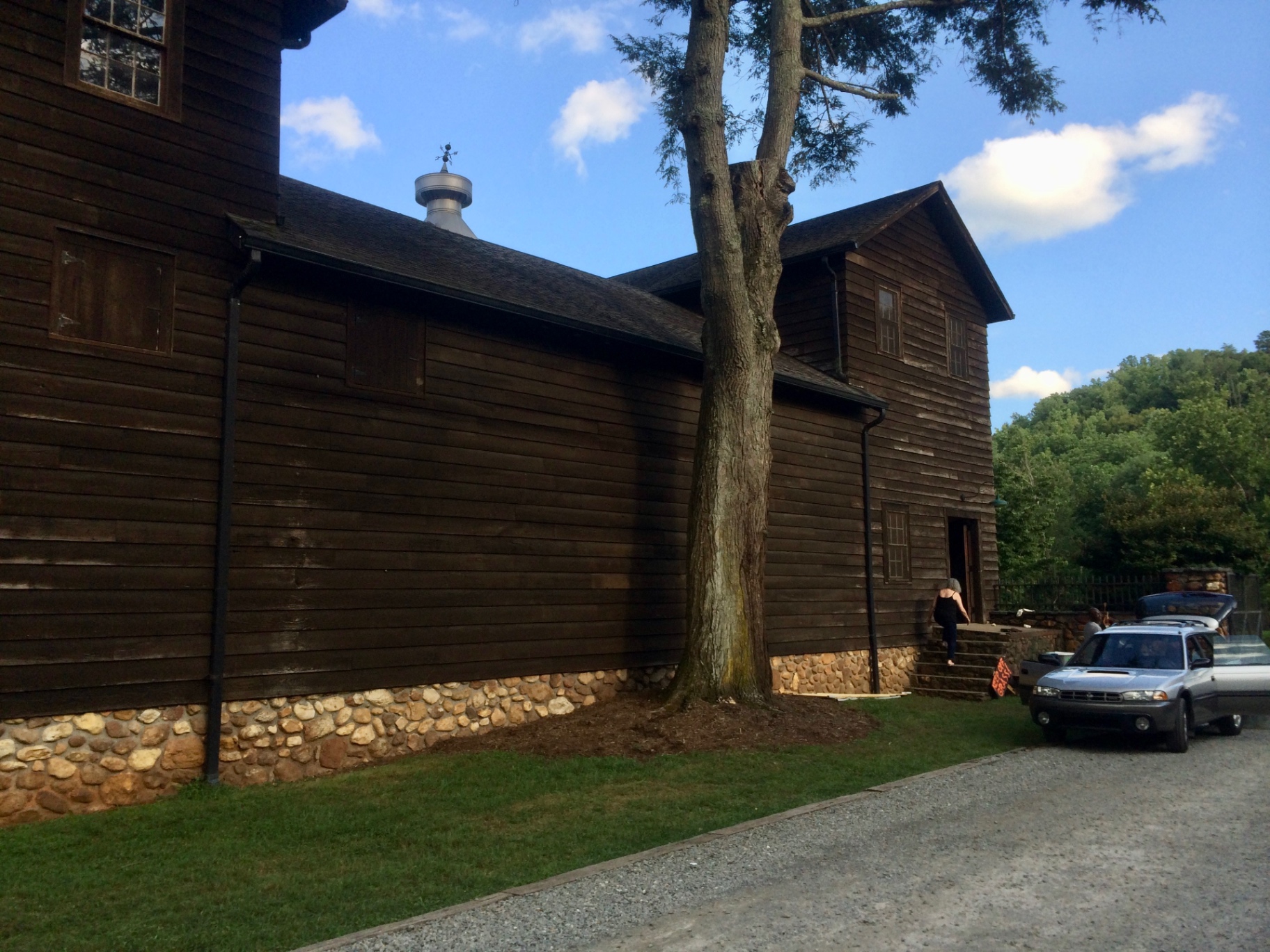The Mill House at Devotion — a tall dark chestnut-clad building on a river-rock foundation with a metal cupola and weathervane