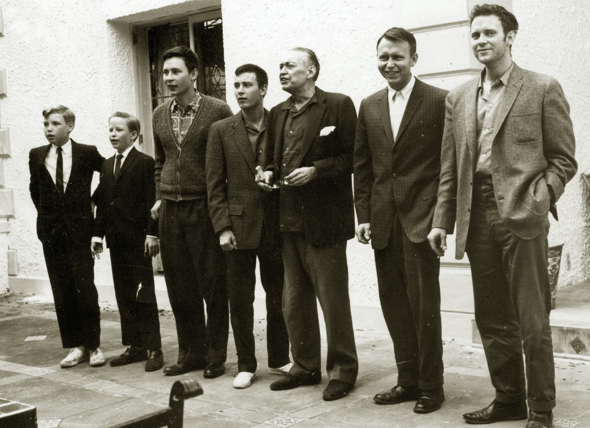 Dick Reynolds standing outdoors with all of his sons — Patrick, Michael, Will, Zach, John, and Josh — in a row against a white stucco wall