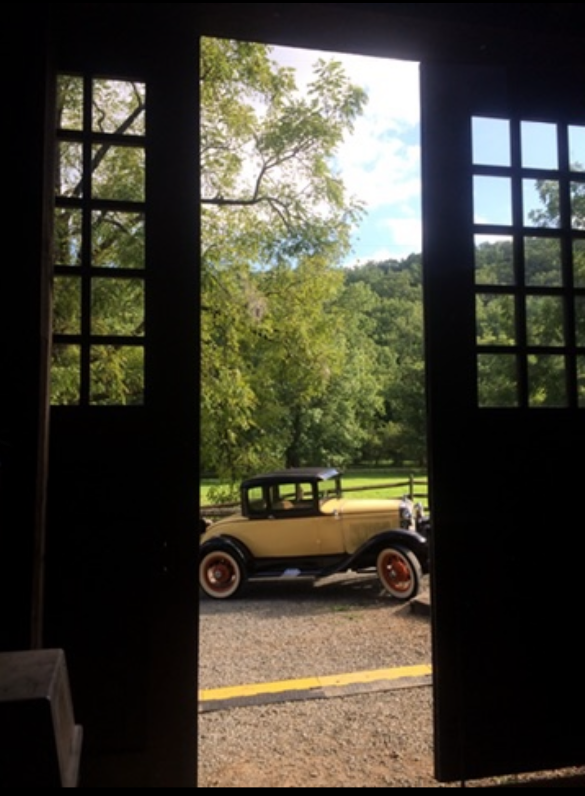 A cream-colored vintage coupe framed through the open double doors of a Devotion outbuilding
