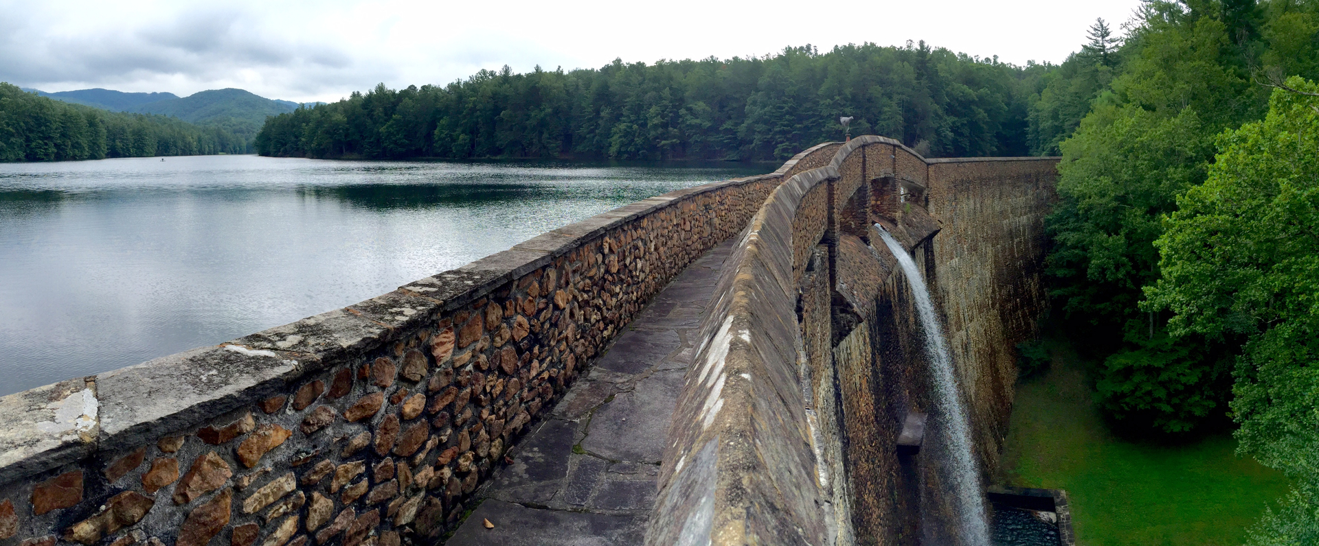 The stone crest walkway of the Devotion dam, with the lake on one side and the spillway falling away on the other