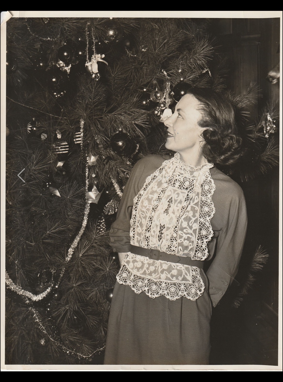 Elizabeth "Blitz" Dillard Reynolds in a lace-collared dress standing beside a decorated Christmas tree, looking up at the ornaments