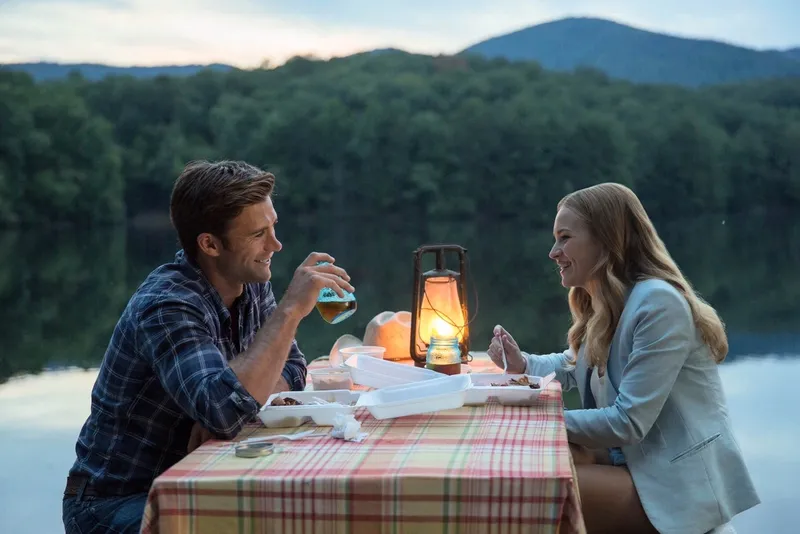 A still from The Longest Ride showing two characters at a lantern-lit table beside a mountain lake