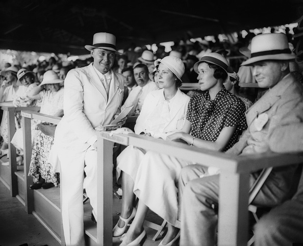 Dick and Blitz Reynolds in summer whites and cloche hats seated in a crowded grandstand at the Kentucky Derby in the 1930s