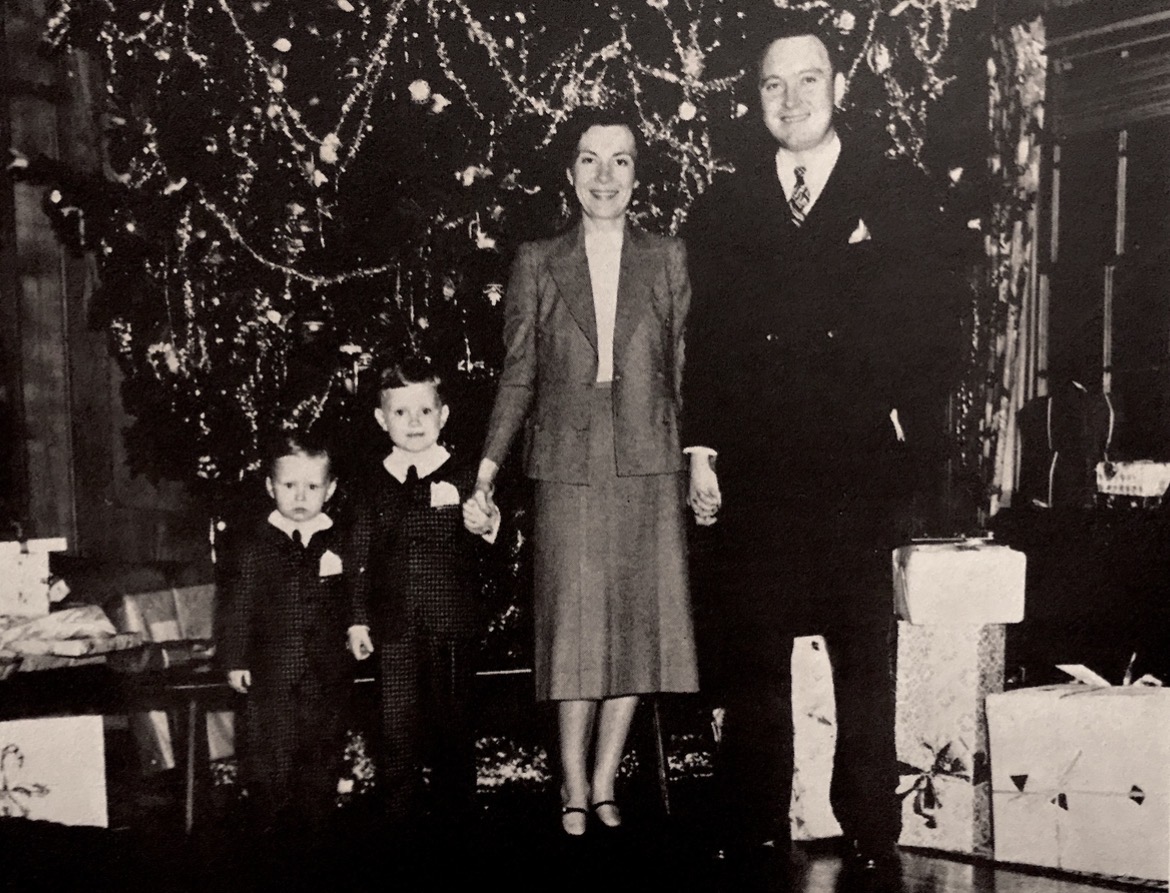 Dick and Blitz Reynolds with their two young sons in front of a decorated Christmas tree surrounded by wrapped presents